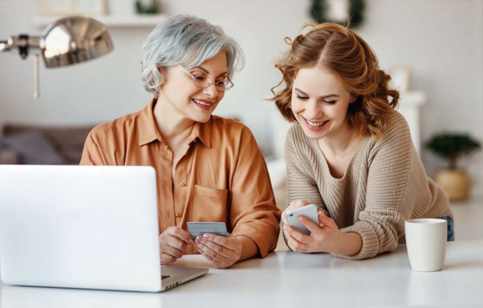 Young,Daughter,With,Smartphone,Smiling,And,Showing,In,Laptop,To